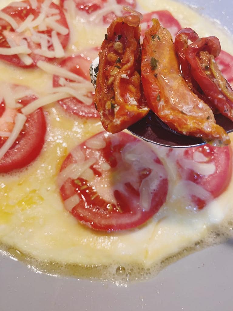 Tomato slices and cheese being added to a cooking omelette.